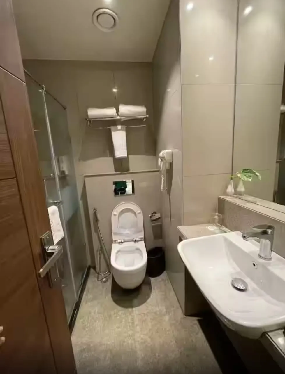 A clean attached bathroom with a glass shower screen and basin — Shree Chaitanya Gaudiya Math, Puri