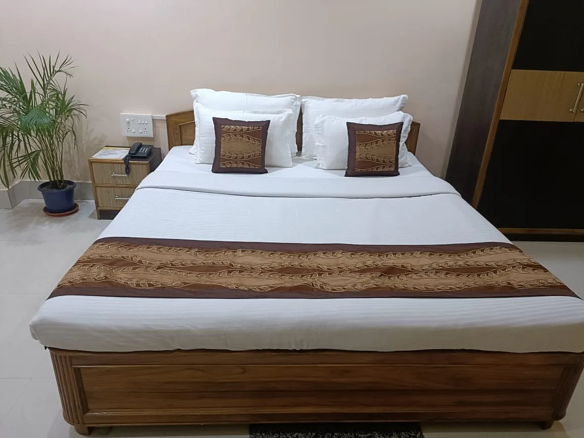 A non-air-conditioned double room with a wooden bed, patterned runner and bedside table — Shree Chaitanya Gaudiya Math, Puri